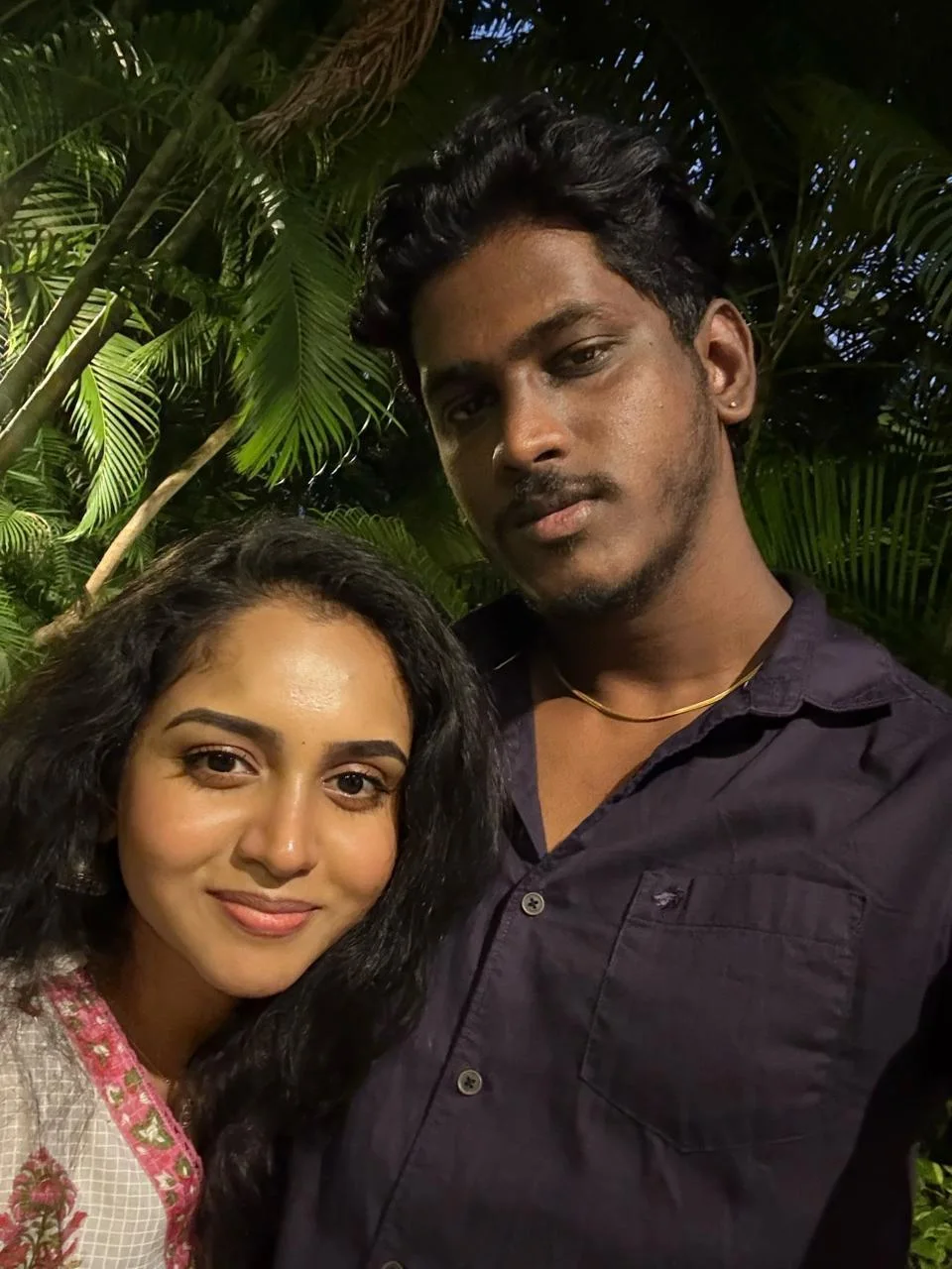 A close selfie of a couple outdoors at night with soft greenery in the background